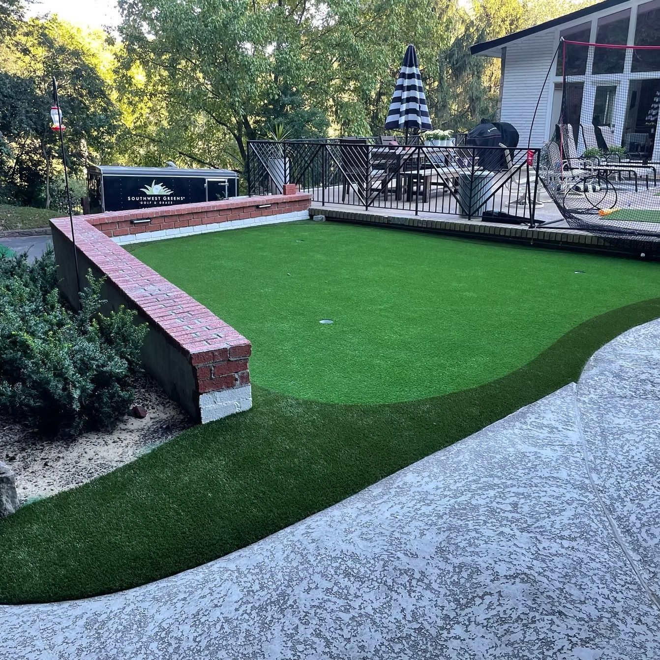 Artificial turf putting green in a backyard, bordered by a brick wall and patio.