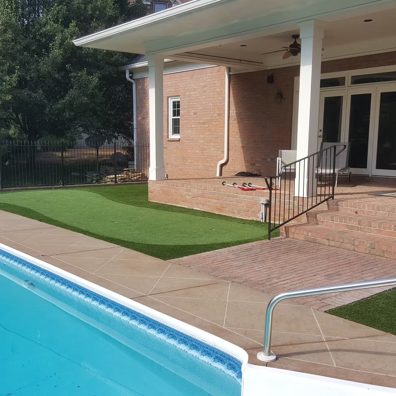 Swimming pool with patio, putting green, and brick house.