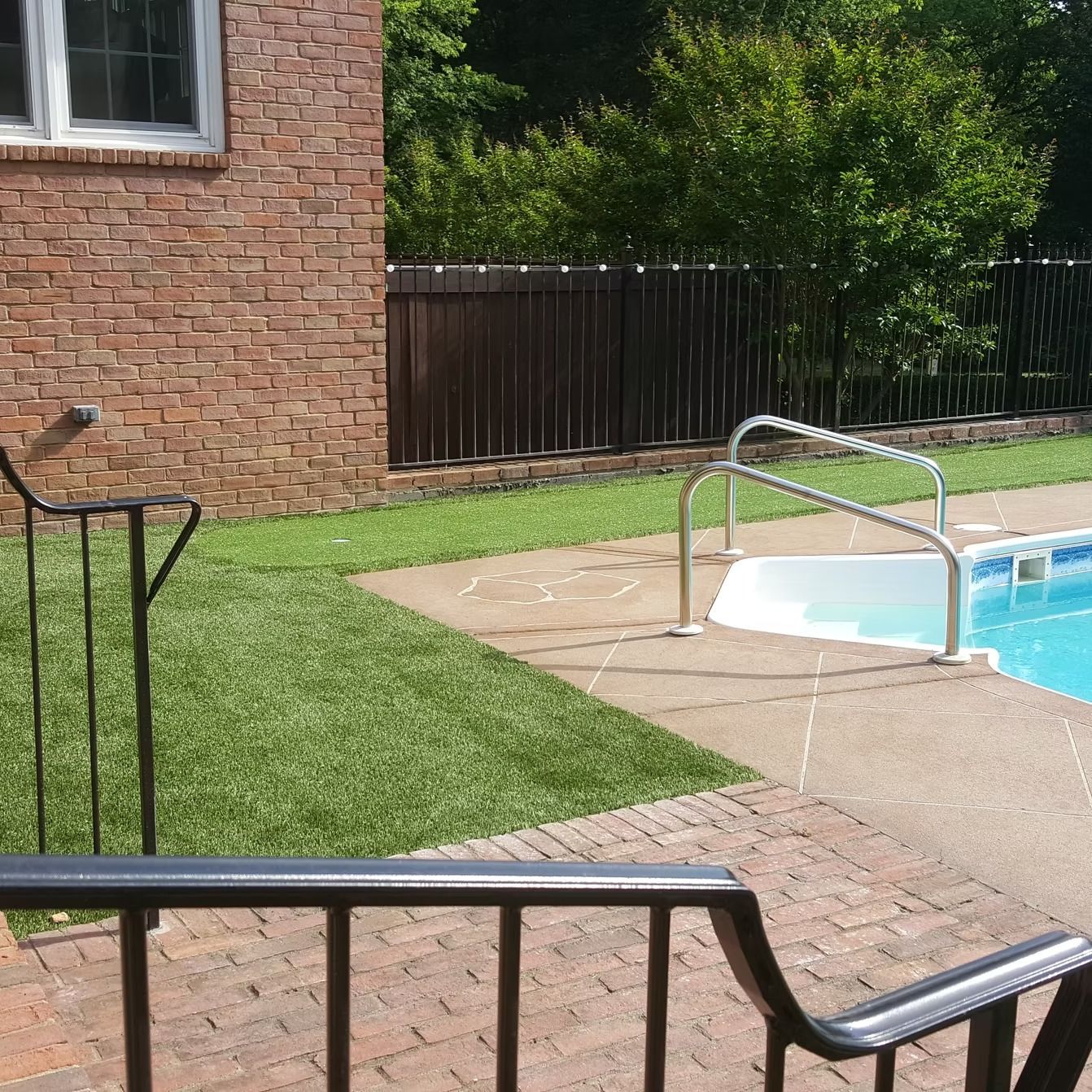 Brick house beside a pool with grass and a black fence.