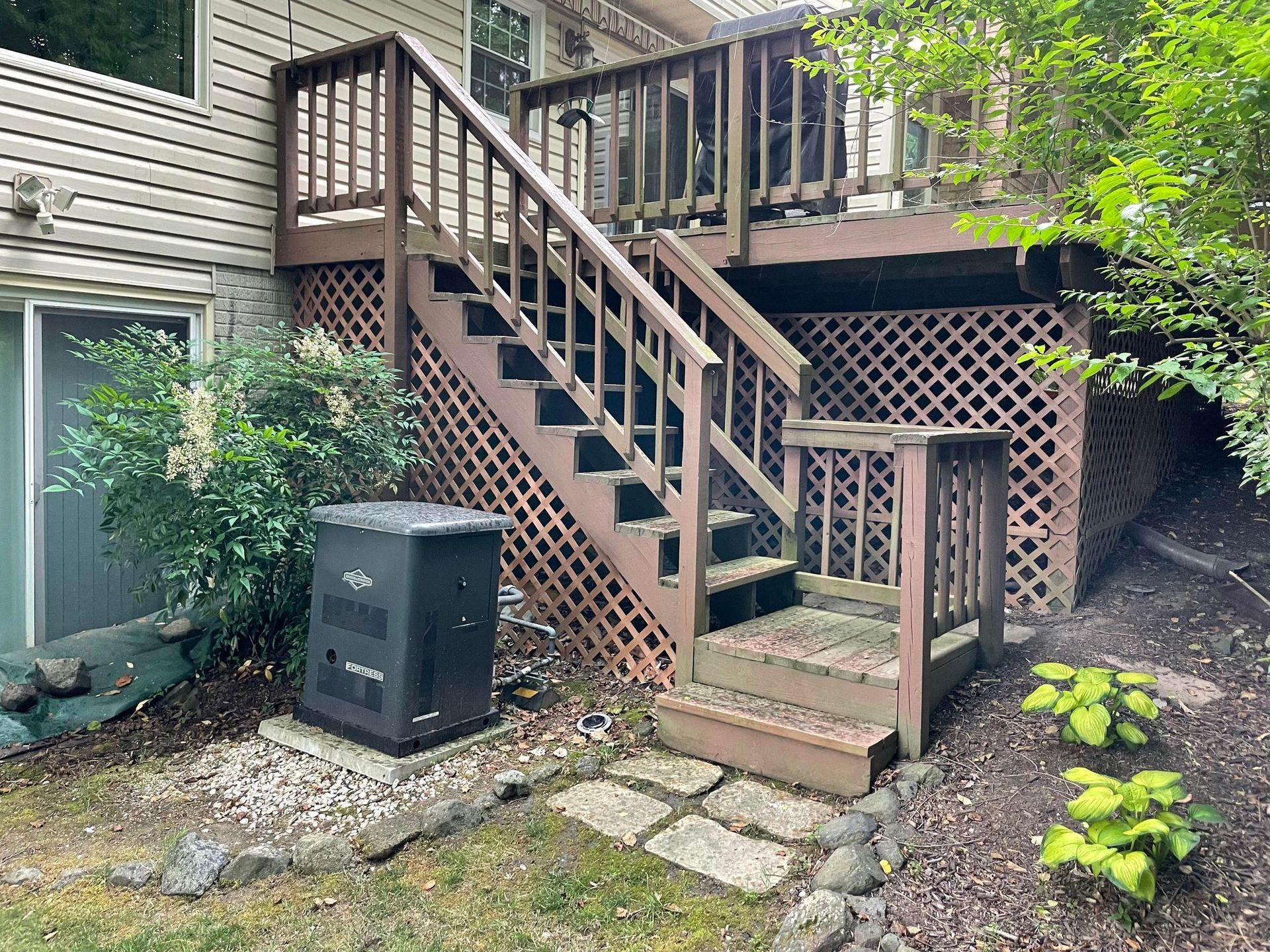 A deck with stairs leading up to it and a generator in the backyard.