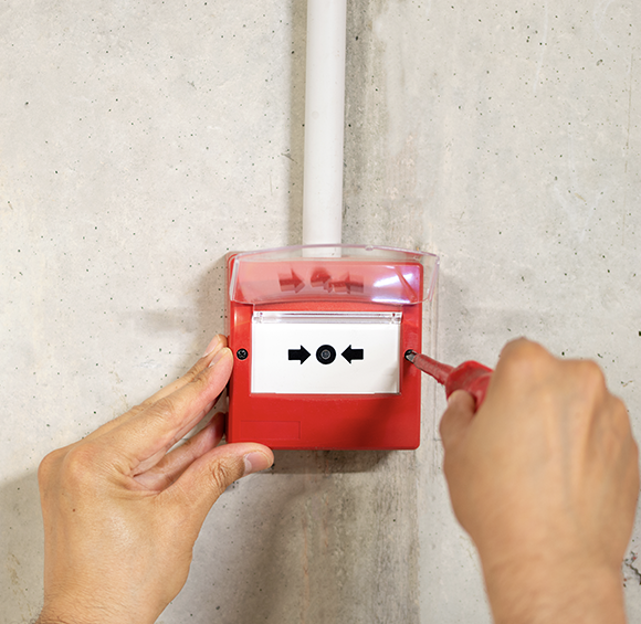 A person is fixing a fire alarm with a screwdriver.