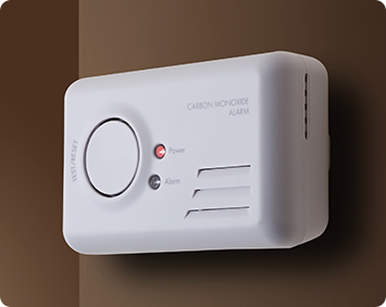A white carbon monoxide alarm is mounted on a brown wall