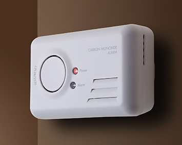 A white carbon monoxide alarm is mounted on a brown wall
