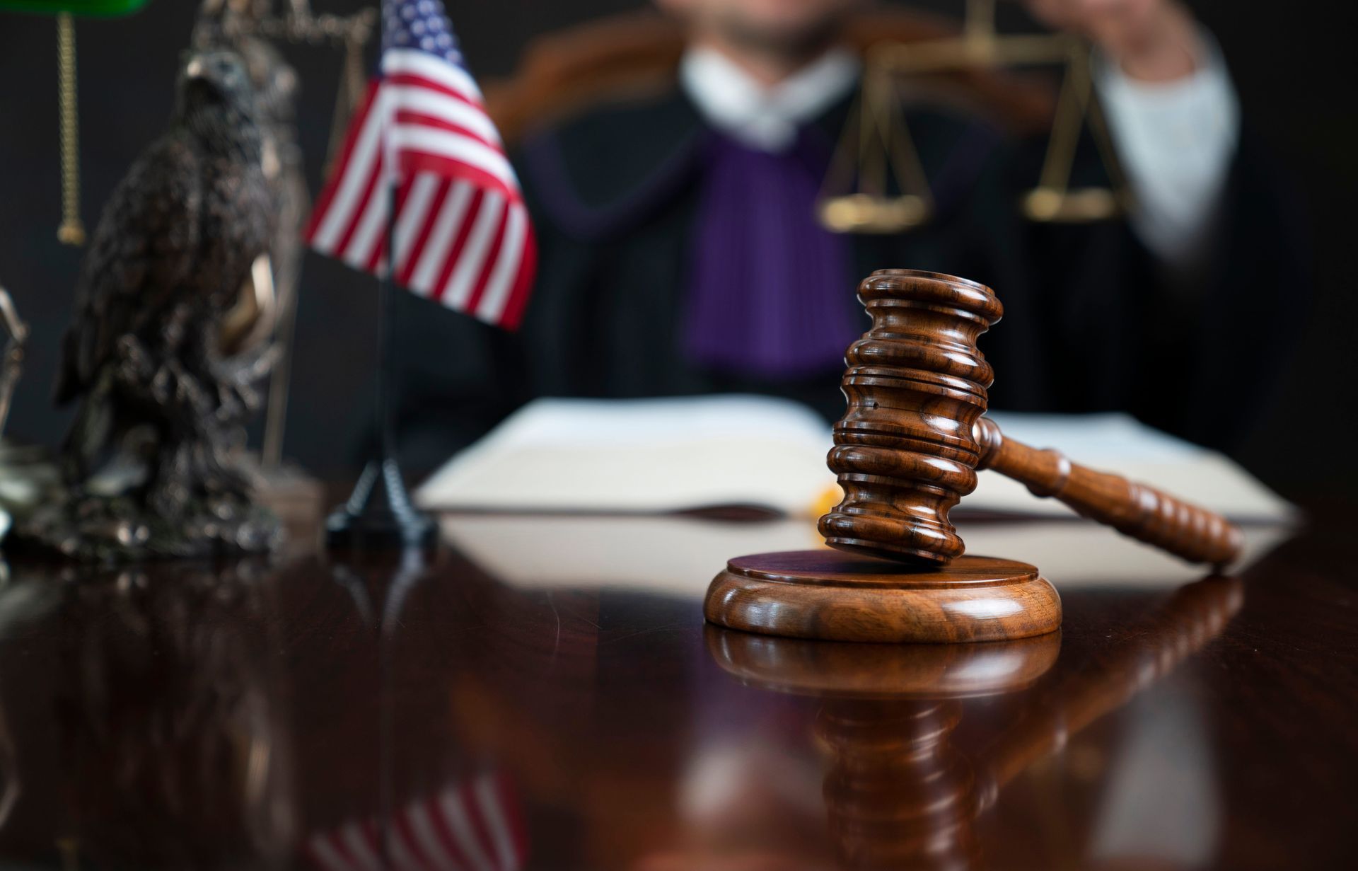 Judge’s gavel on a courtroom table with a U.S. flag and scales of justice in the background
