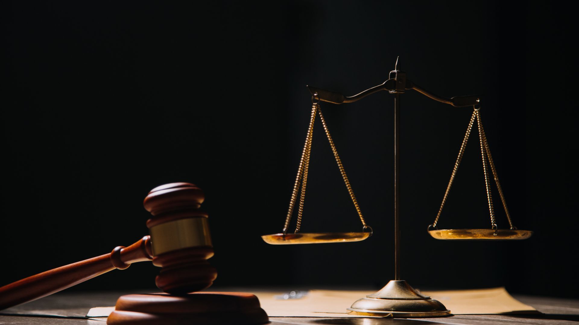 Wooden gavel beside a golden scale of justice on a dark background, suggesting a legal setting.
