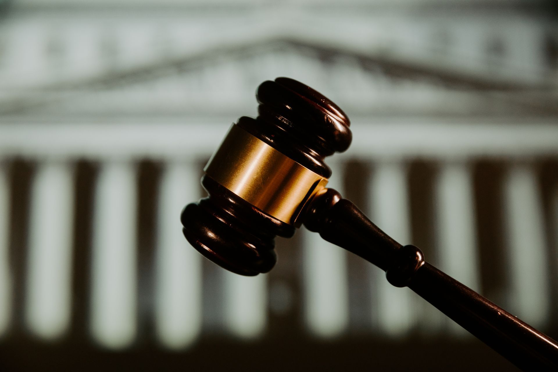 Gavel with gold band in front of a blurred courthouse facade.