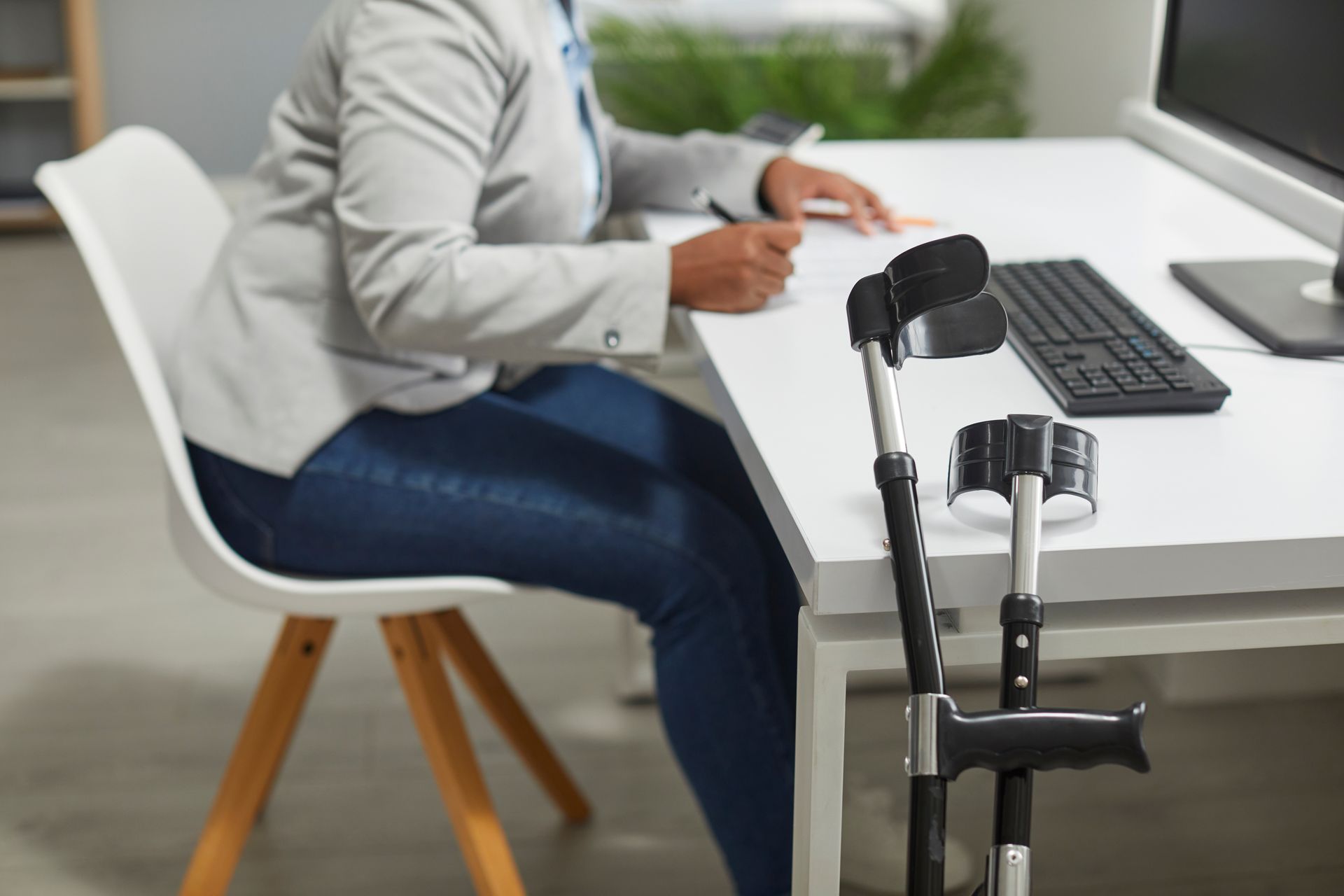 Woman at desk, writing, crutches propped nearby; office setting.