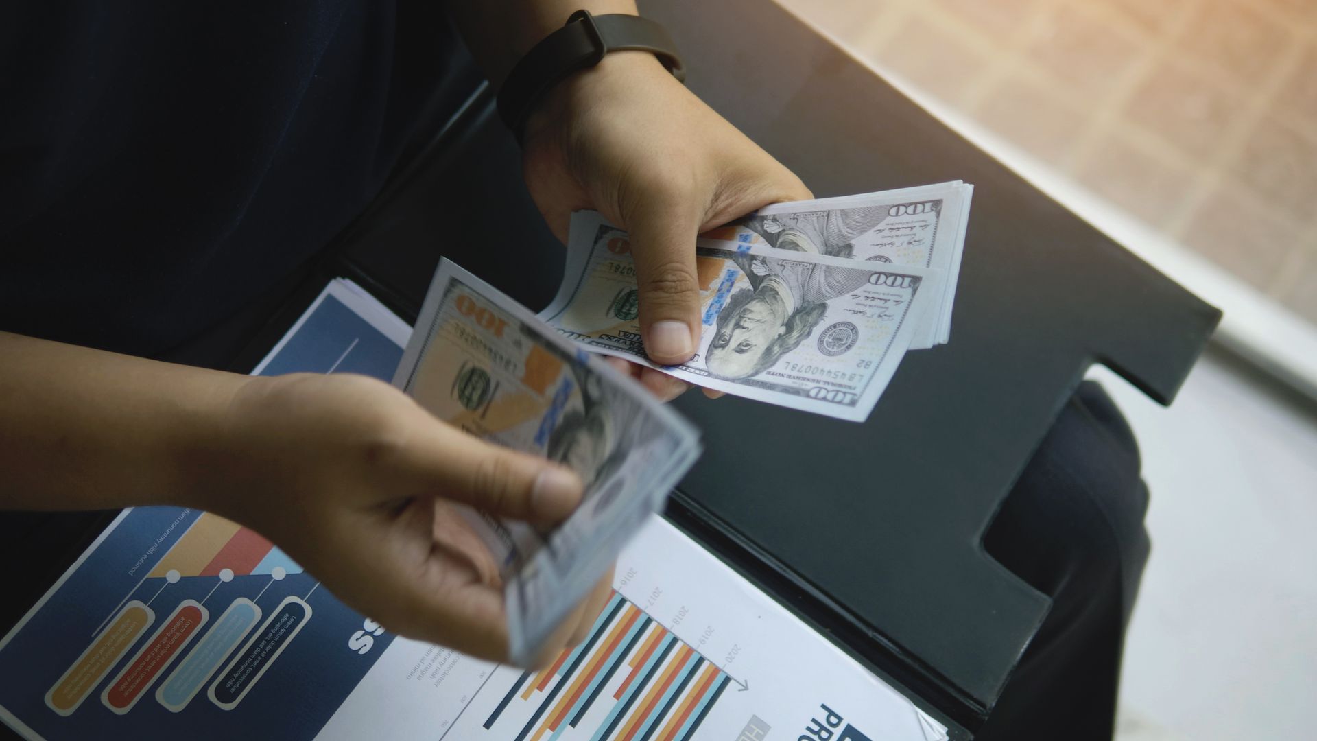 Person counting US dollar bills over a financial report.