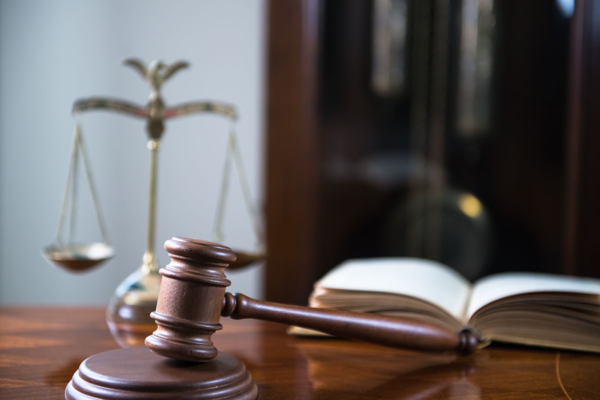 A wooden gavel resting on a desk, with a golden balance scale and an open legal book 