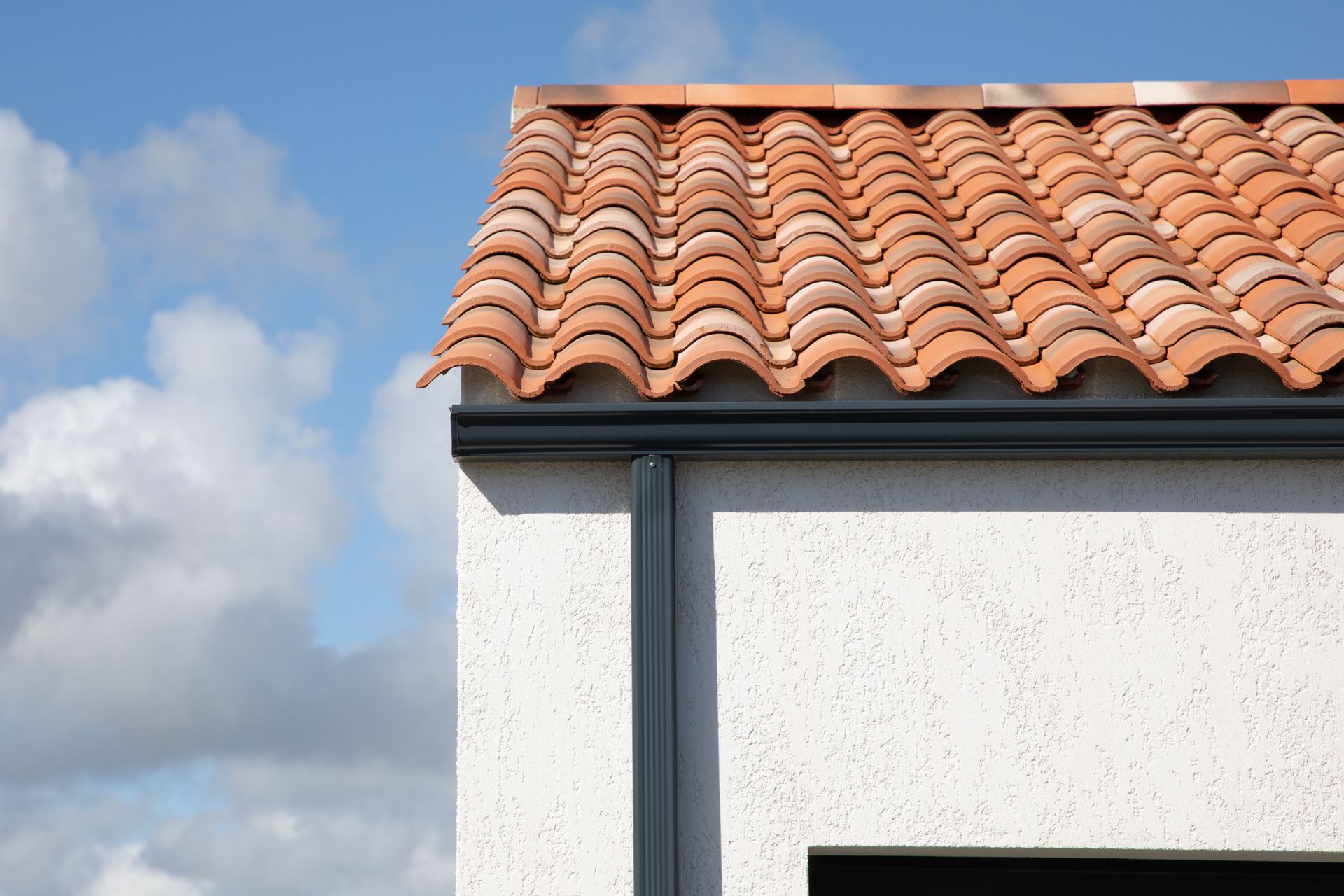 Clay tile roof on a white stucco building against a partly cloudy sky.