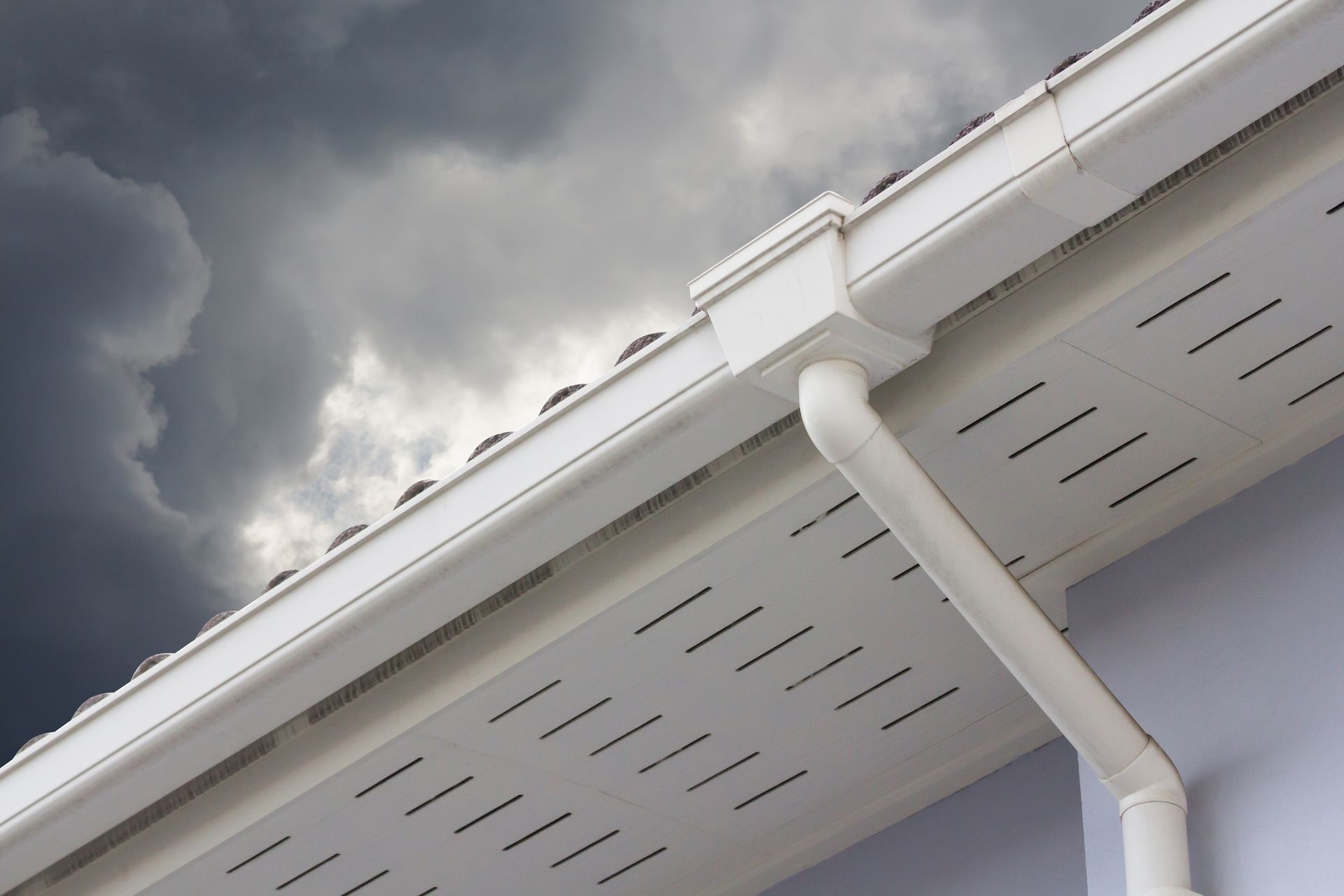 White roof guttering with downspout, against a cloudy sky.