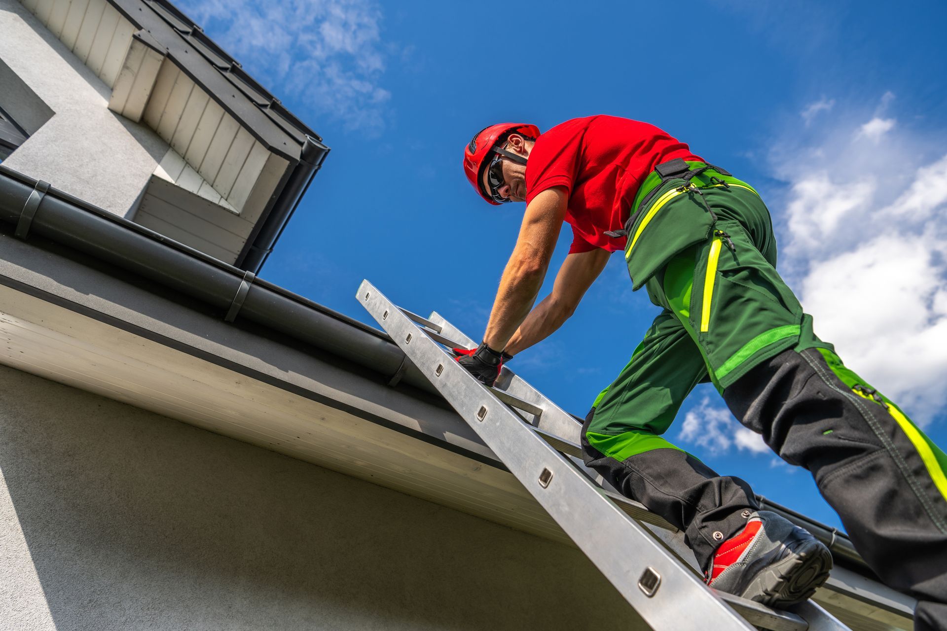 Person in red shirt and helmet climbing a ladder to a roof on a sunny day.