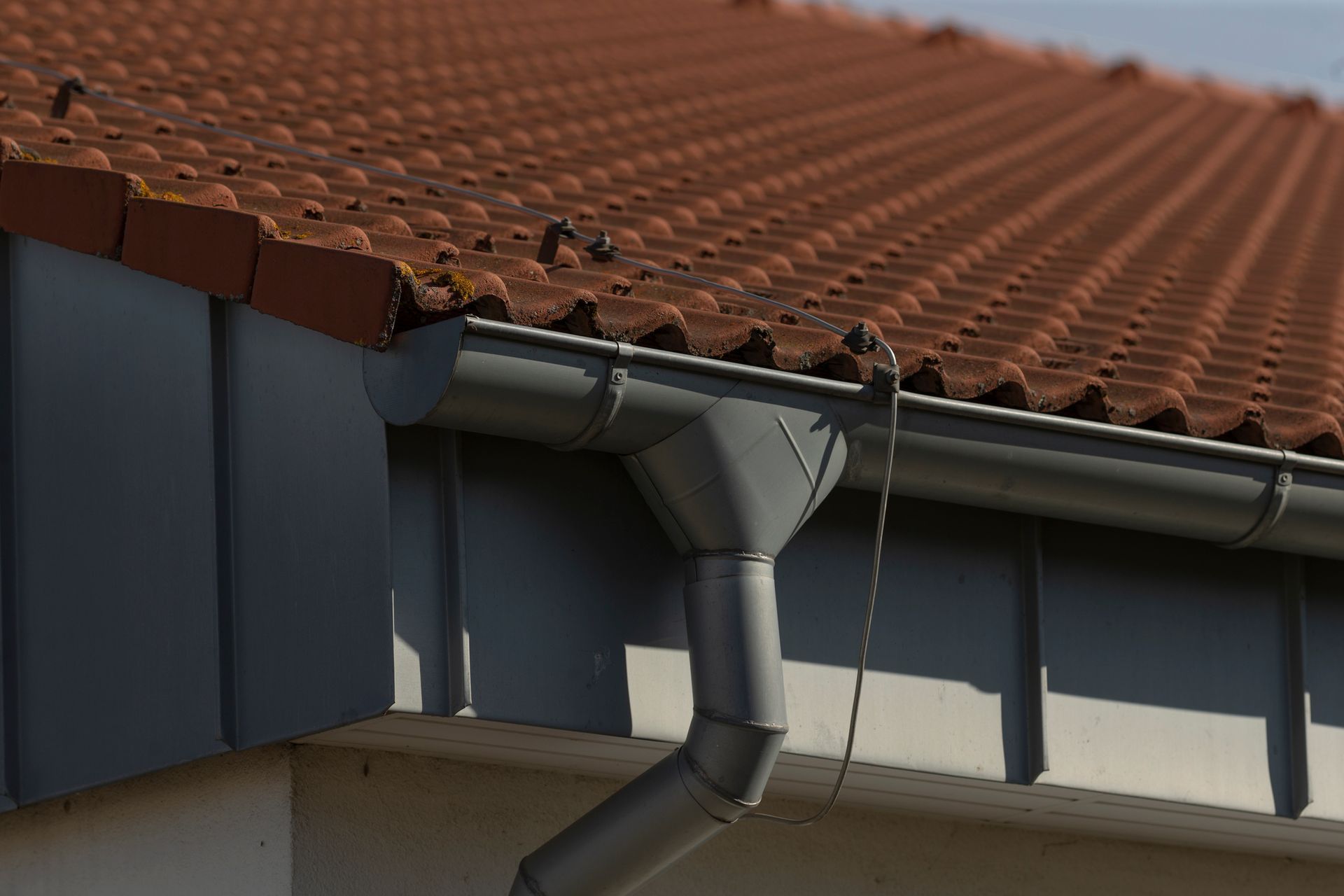 Gray gutter system attached to a red tile roof.