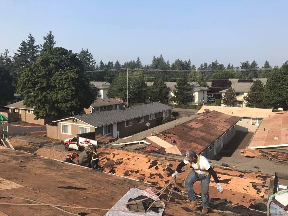 Construction workers removing old roofing on a house with neighborhood in background.