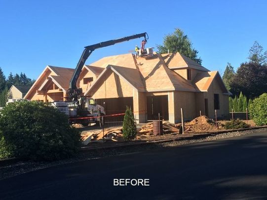 Construction of a two-story house with crane. Workers on roof, garage visible. Daytime, sunny.
