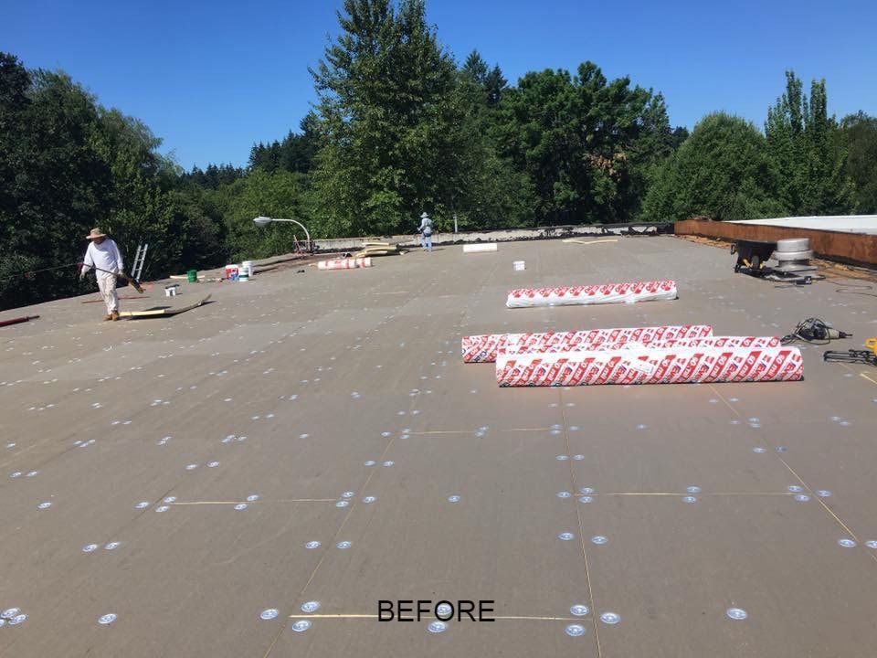 A flat roof with workers, rolls of material, and tools laid out for a re-roofing project on a sunny day.