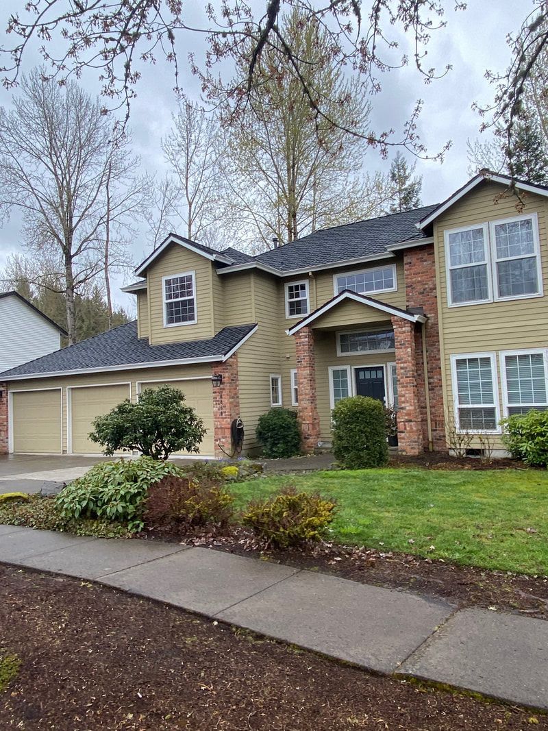 Two-story house with green siding, brick accents, and a green lawn under an overcast sky.