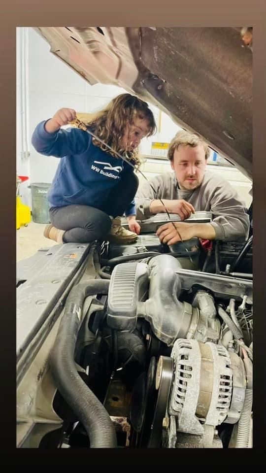 Two people checking car engine. One holding dipstick. Garage setting.