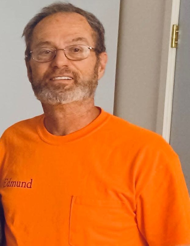 Man with beard and glasses in orange shirt smiles.