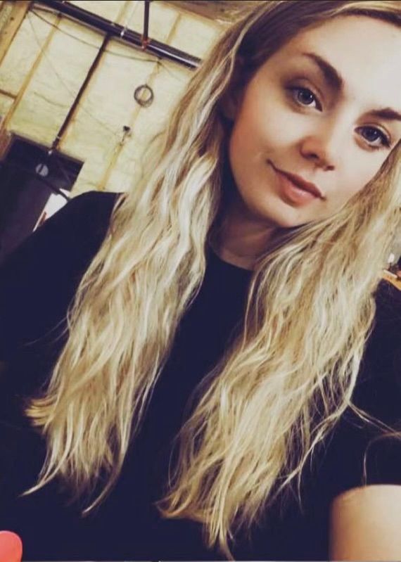 Blonde woman with wavy hair smiles, wearing a black shirt, indoor setting.