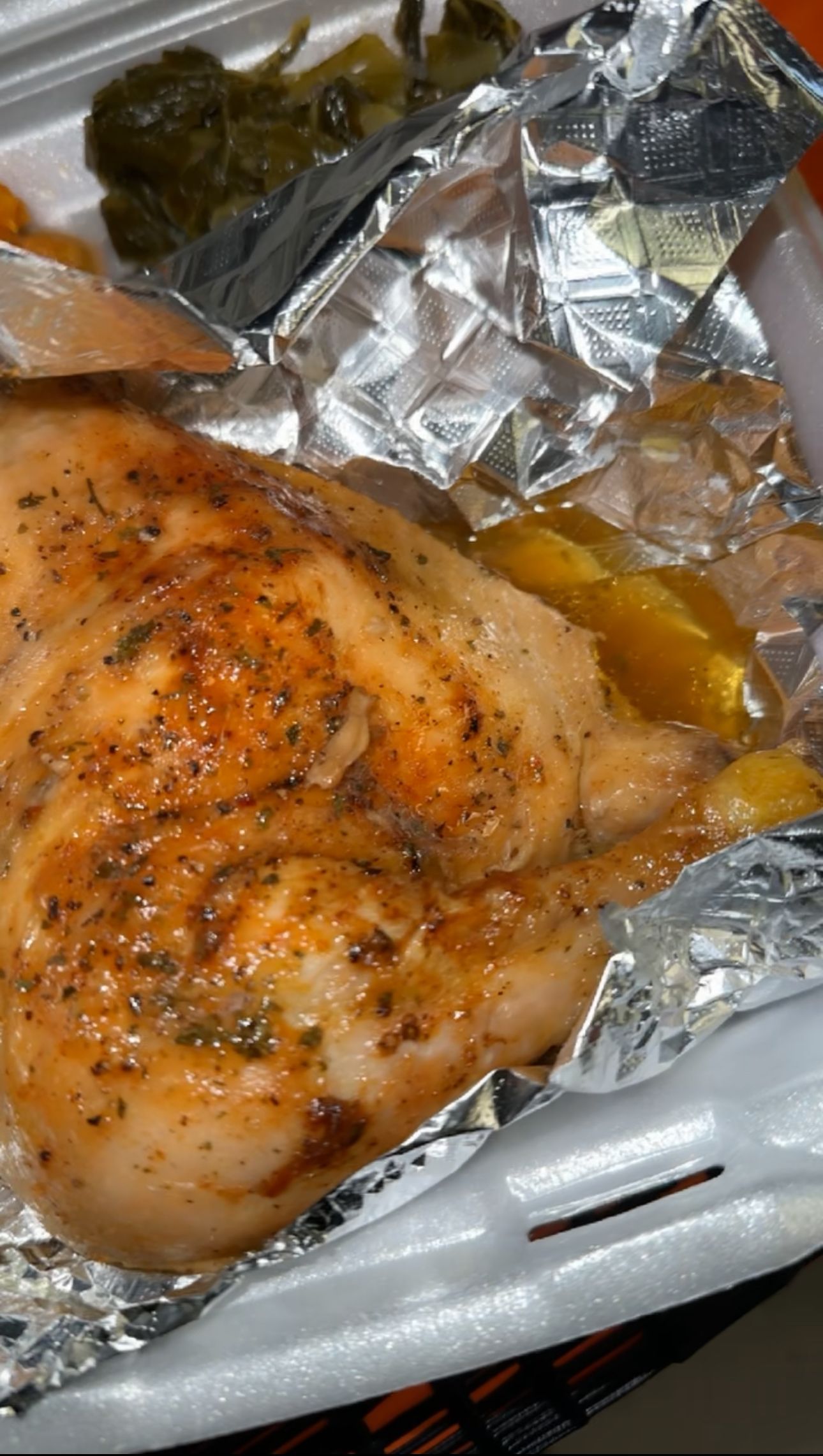 A close up of a piece of chicken wrapped in tin foil in a styrofoam container.