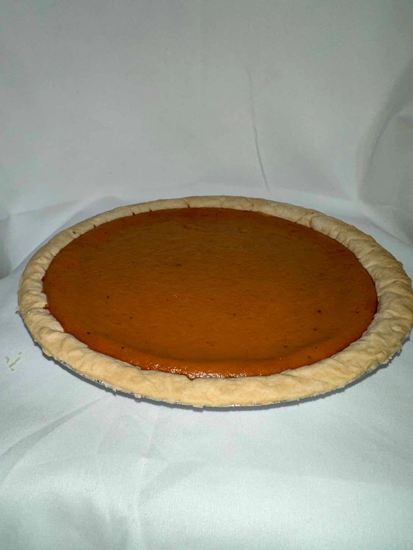 A pumpkin pie is sitting on a white cloth on a table.