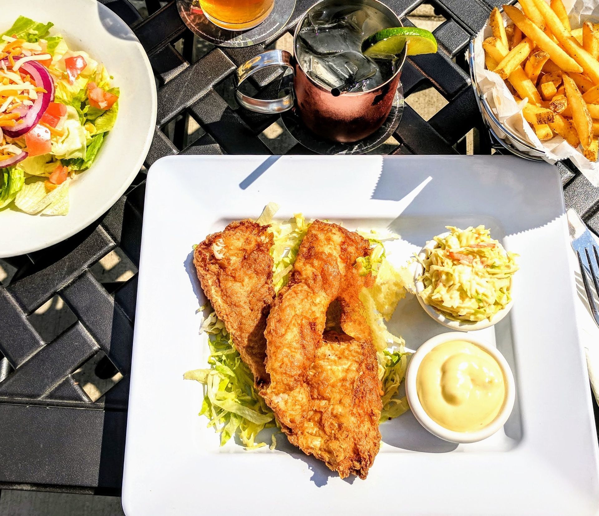 A plate of food is sitting on a table next to a salad and french fries.