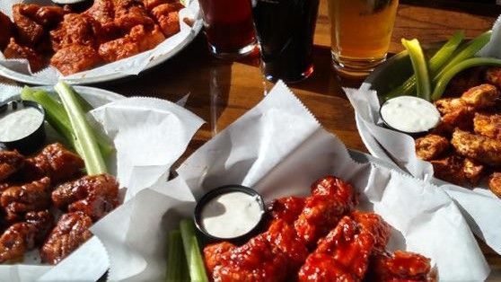 A table topped with plates of chicken wings and a glass of beer.