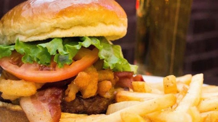 A hamburger and french fries are on a plate next to a glass of beer.