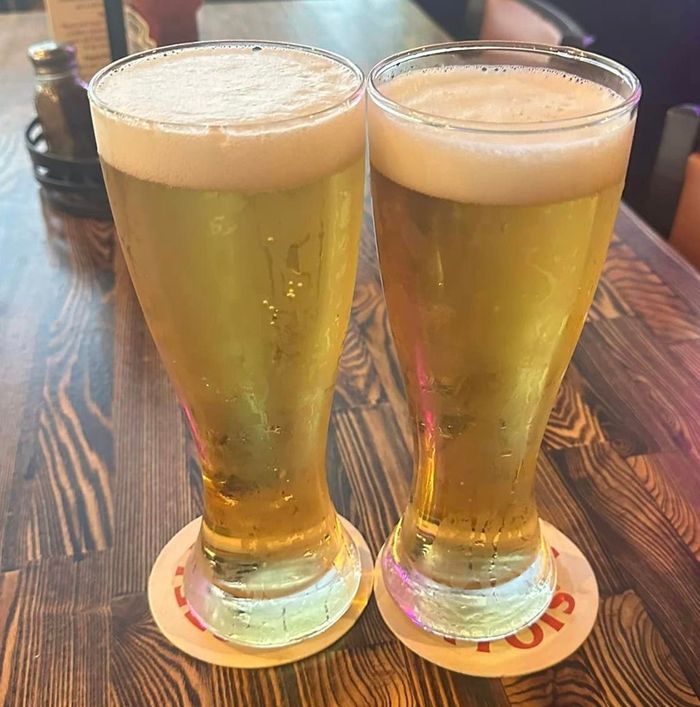 Two glasses of beer are sitting on a wooden table.