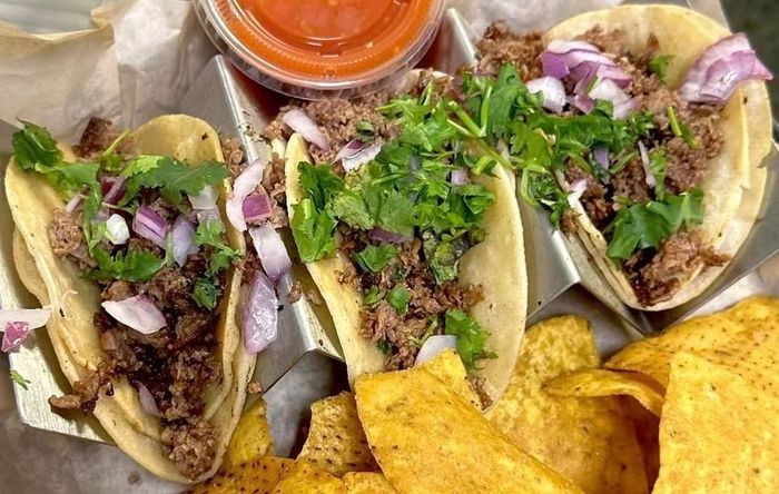 A person is holding a basket of tacos and tortilla chips.