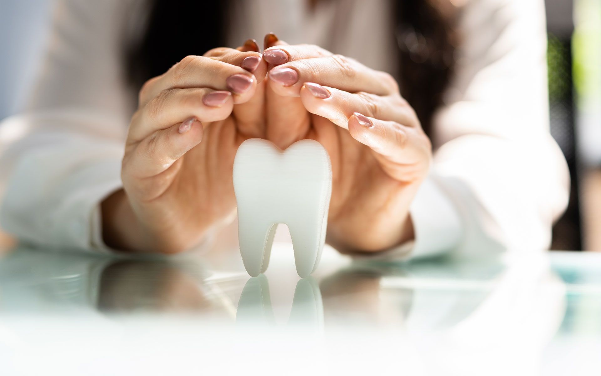 Hands protect a large white tooth on a reflective surface; focus on dental health.