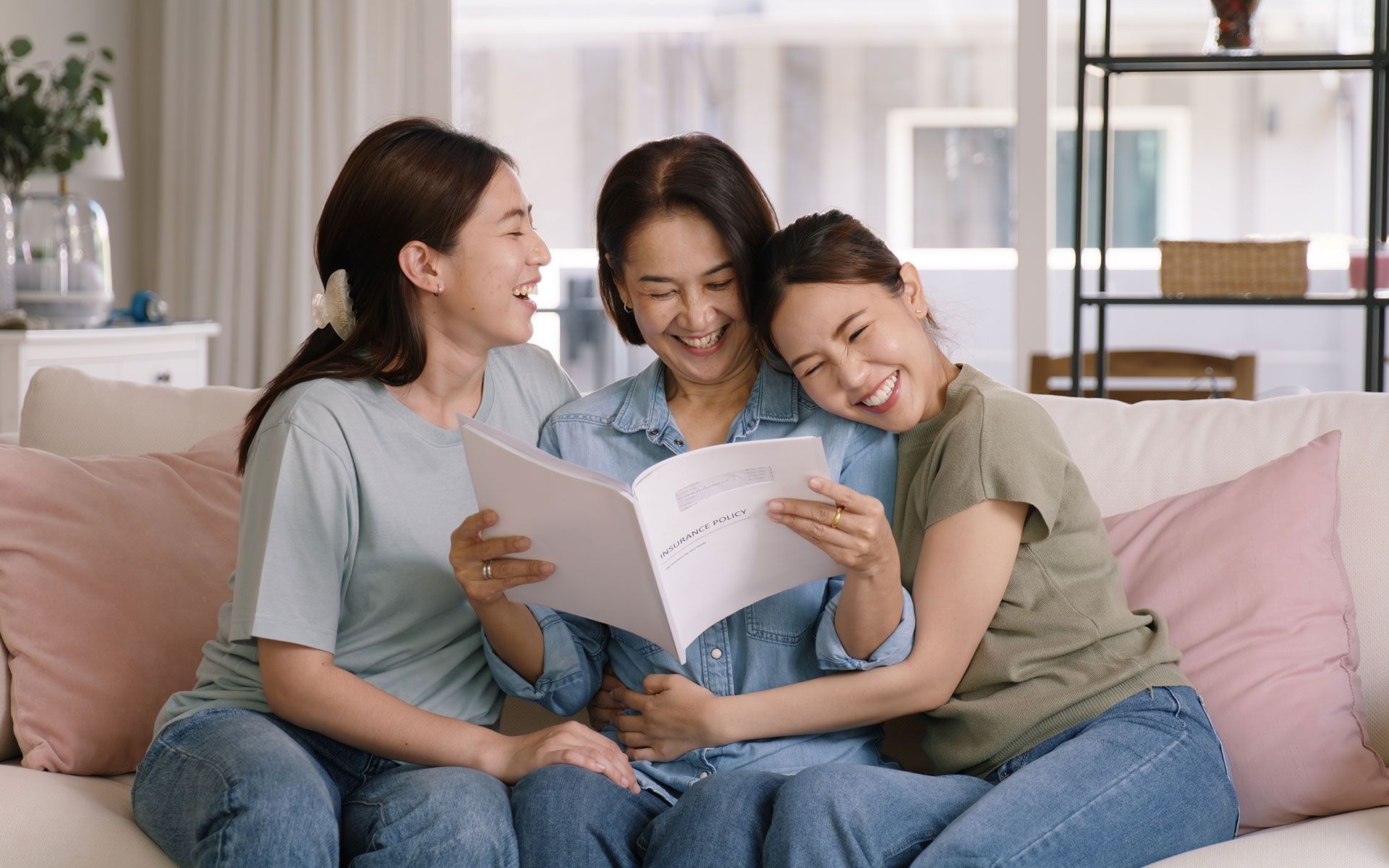 Three smiling women looking at a photo album on a sofa.