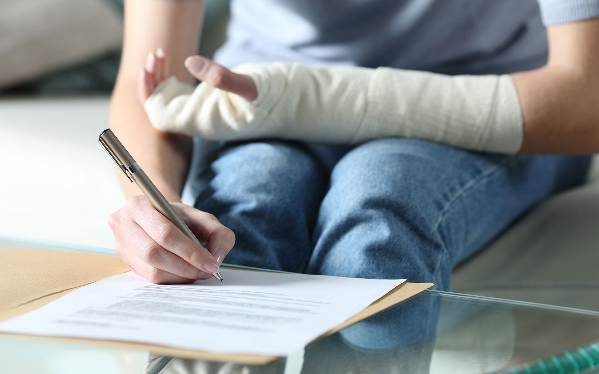 Person with arm in cast signing documents at a glass table.