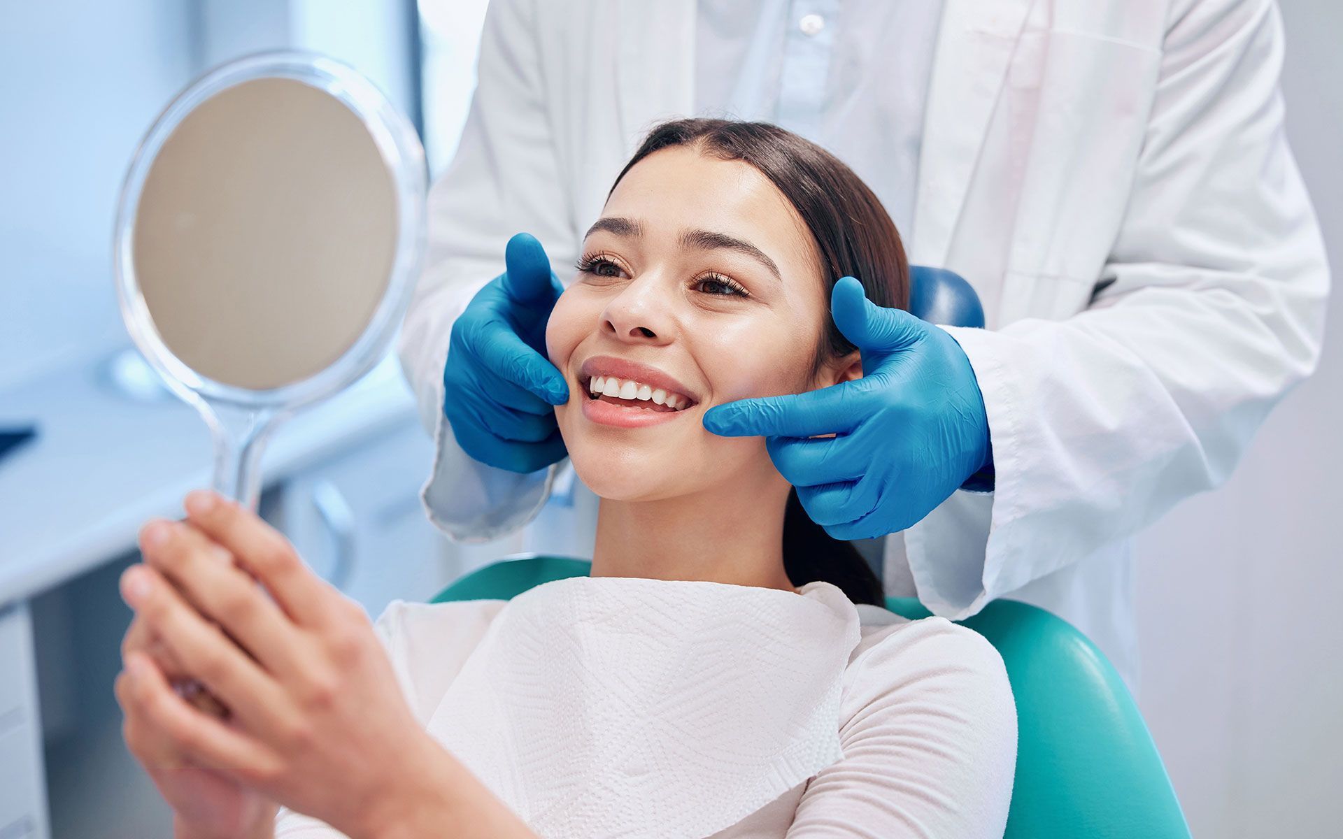 Woman at the dentist smiles, looking in a mirror as the dentist examines her teeth.