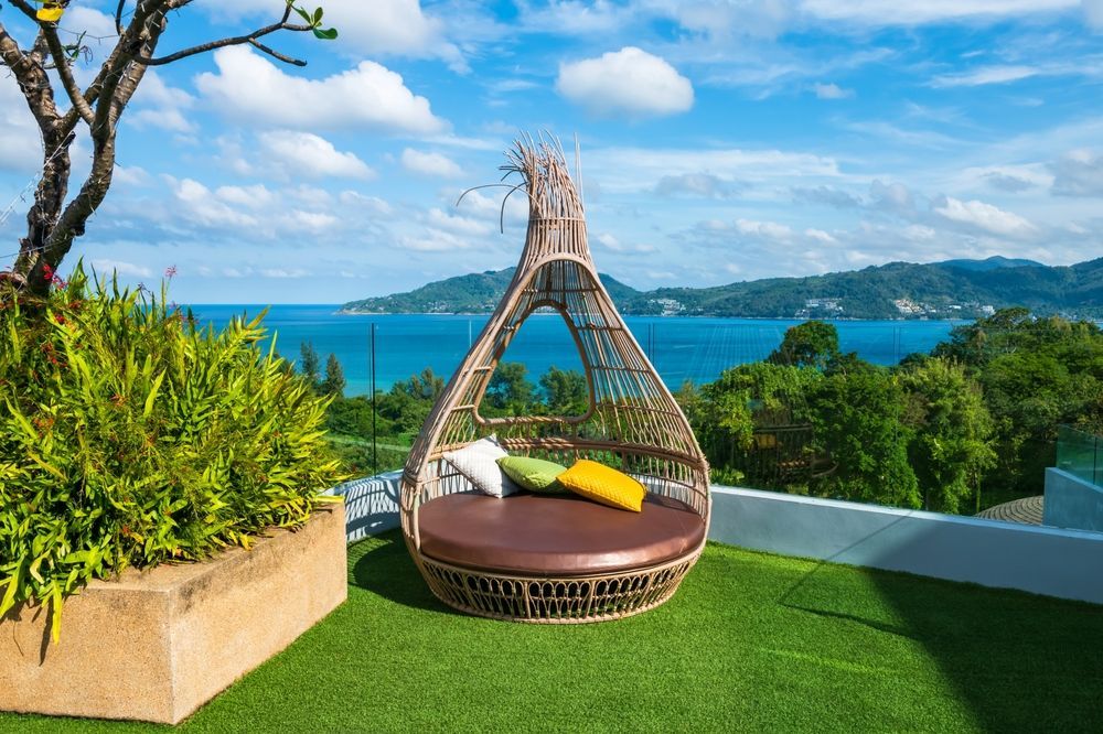 Un letto di vimini è posto in cima a un lussureggiante tetto verde con vista sull'oceano.