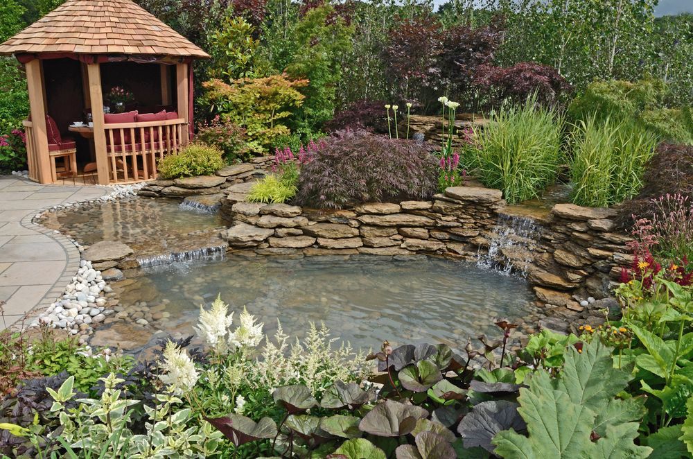 Un gazebo in un giardino con uno stagno e una cascata