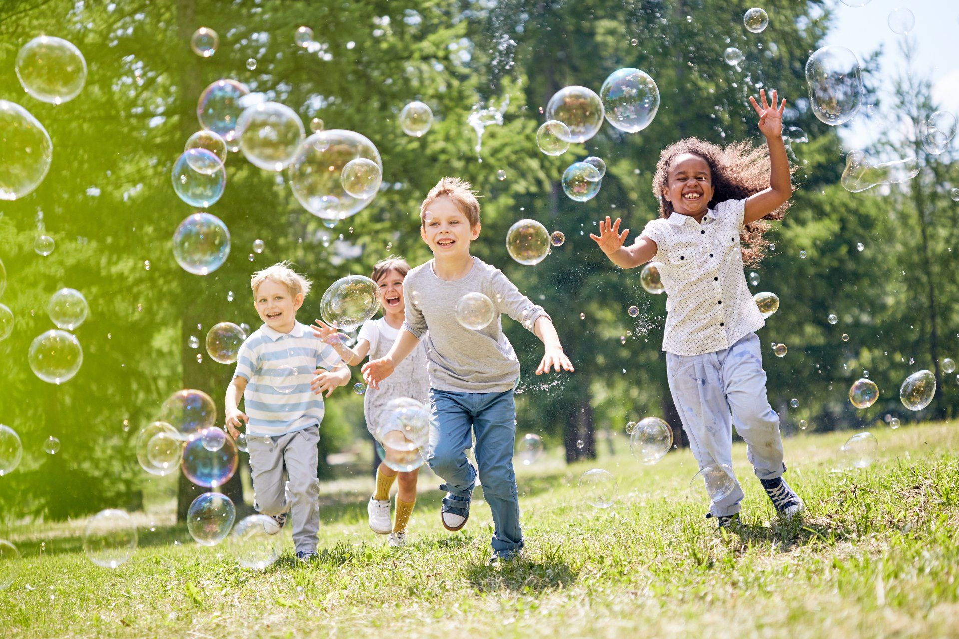 A group of children are chasing bubbles across a grassy field
