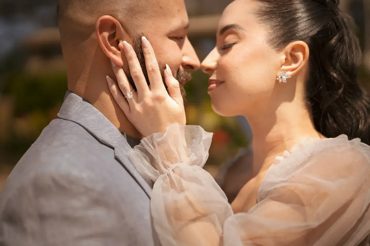 Couple embraces, woman touches man's face, possibly outdoors. Soft focus, warm lighting.