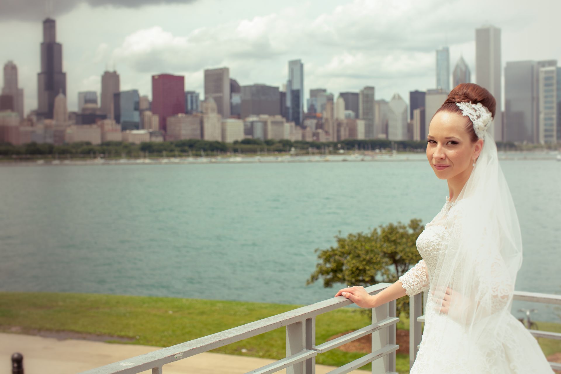 Bride in wedding dress, Chicago skyline in background, overlooking water.