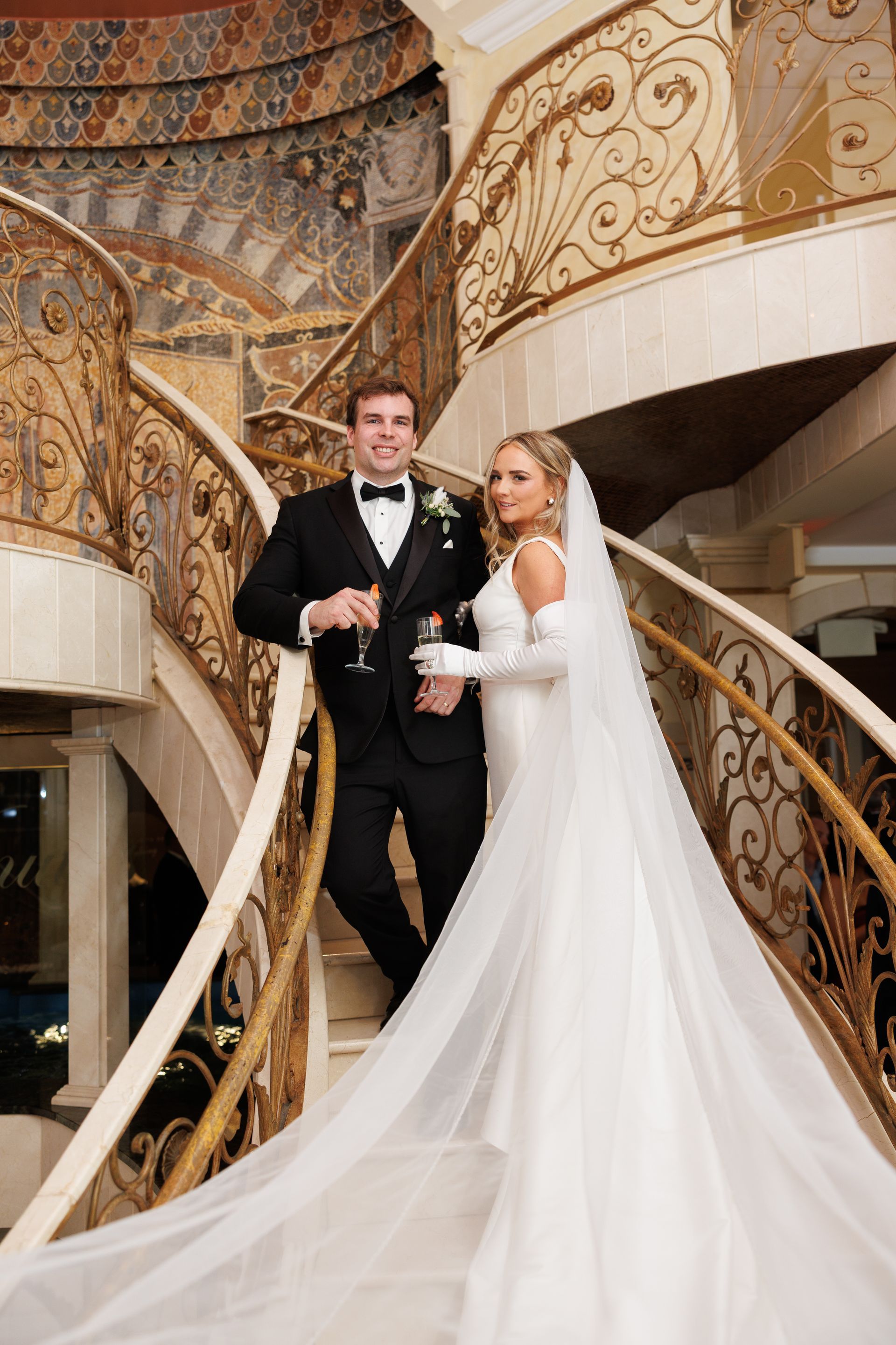 Two people toasting champagne glasses. City background, wearing a white suit and dress.