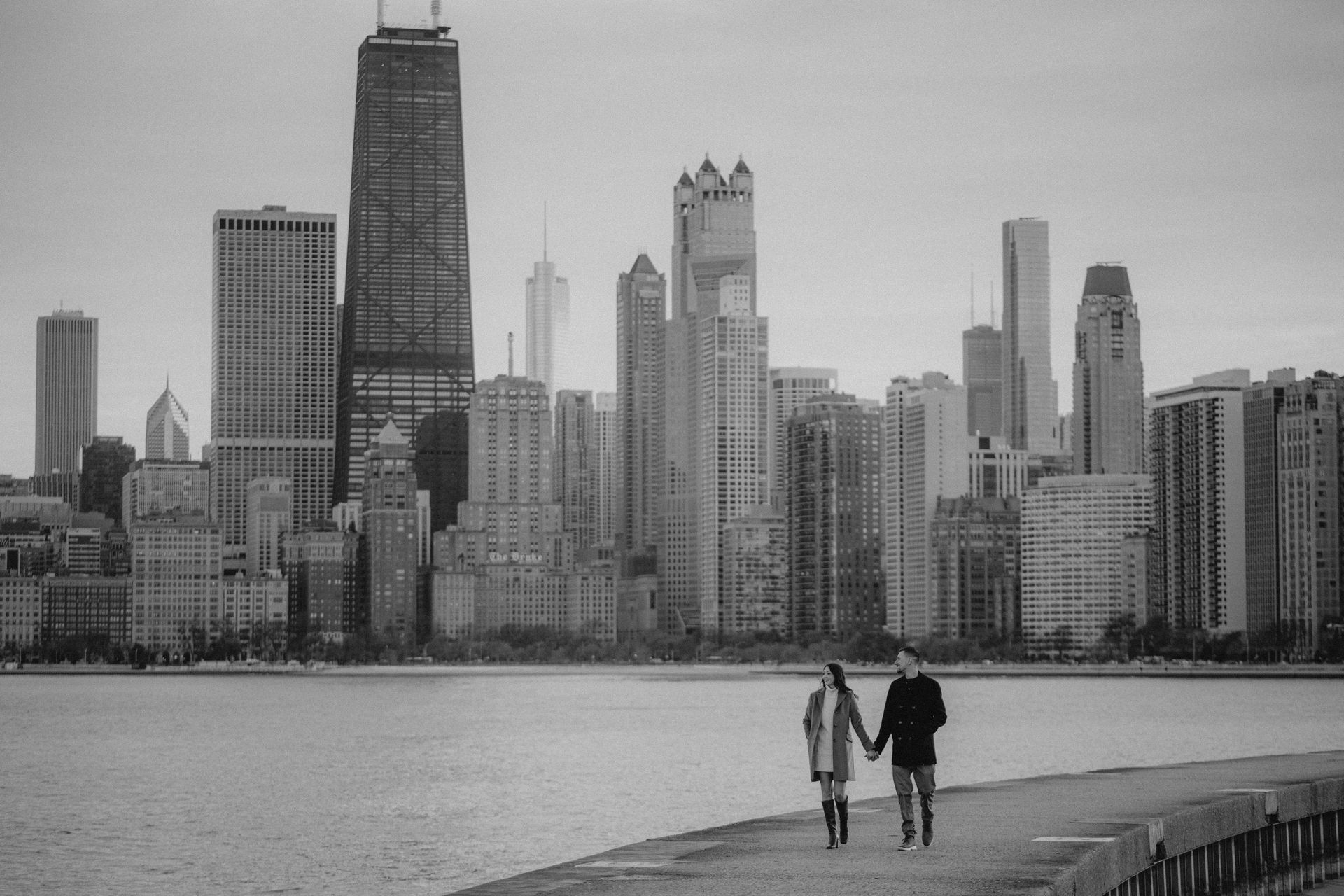 Two smiling women embrace; one in red dress, one in pink, posing by a mosaic wall.