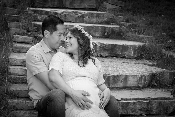 Couple sitting on stone steps, woman pregnant, man touching her belly, both smiling.
