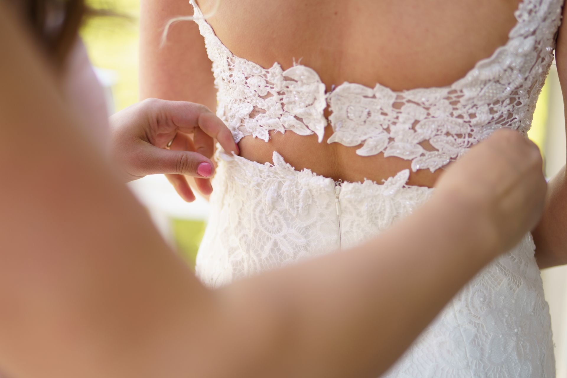Woman's back in white lace wedding dress as someone adjusts the dress.