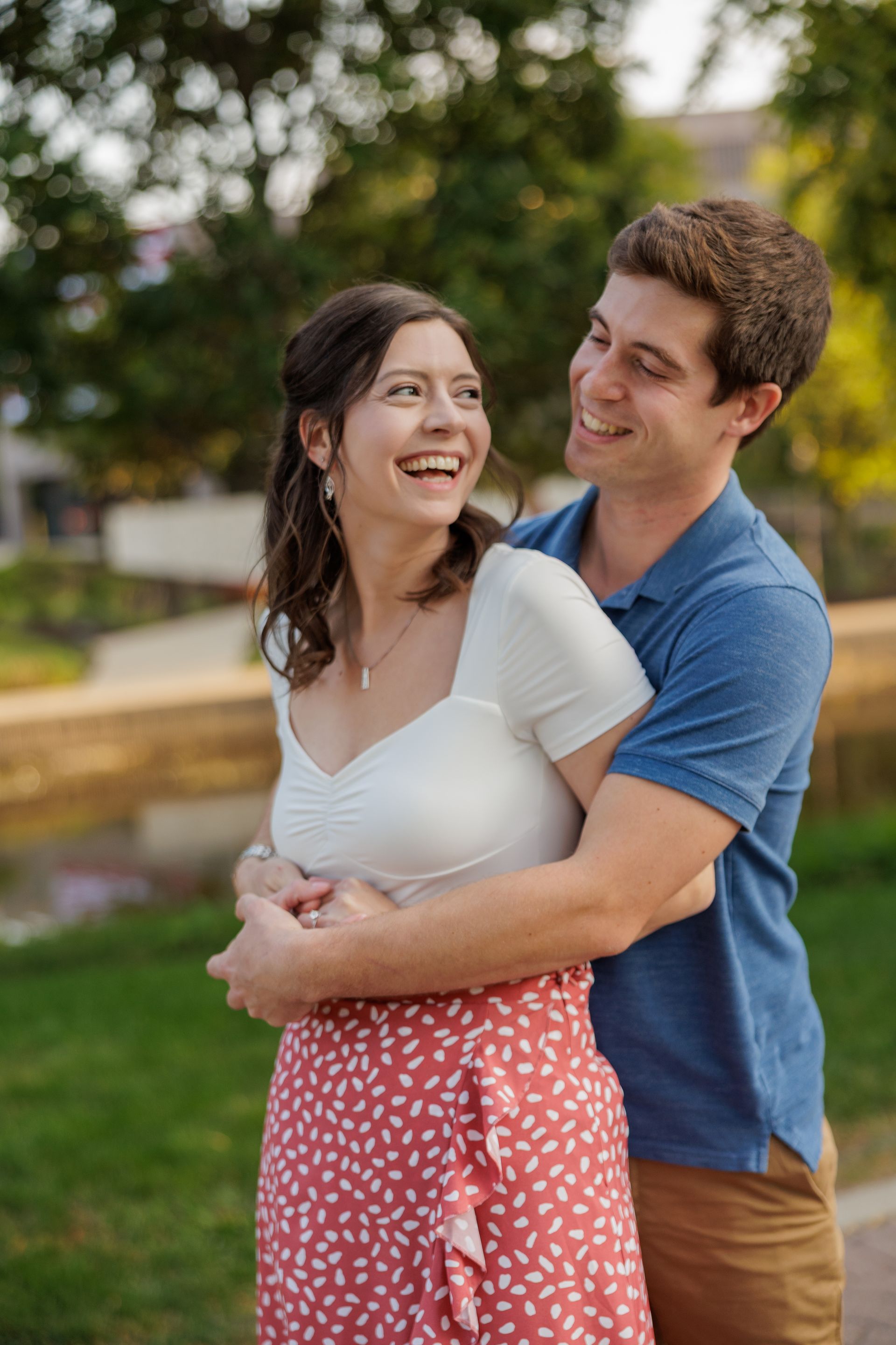 Bride and groom in formal attire, smiling. Interior setting with art and window.