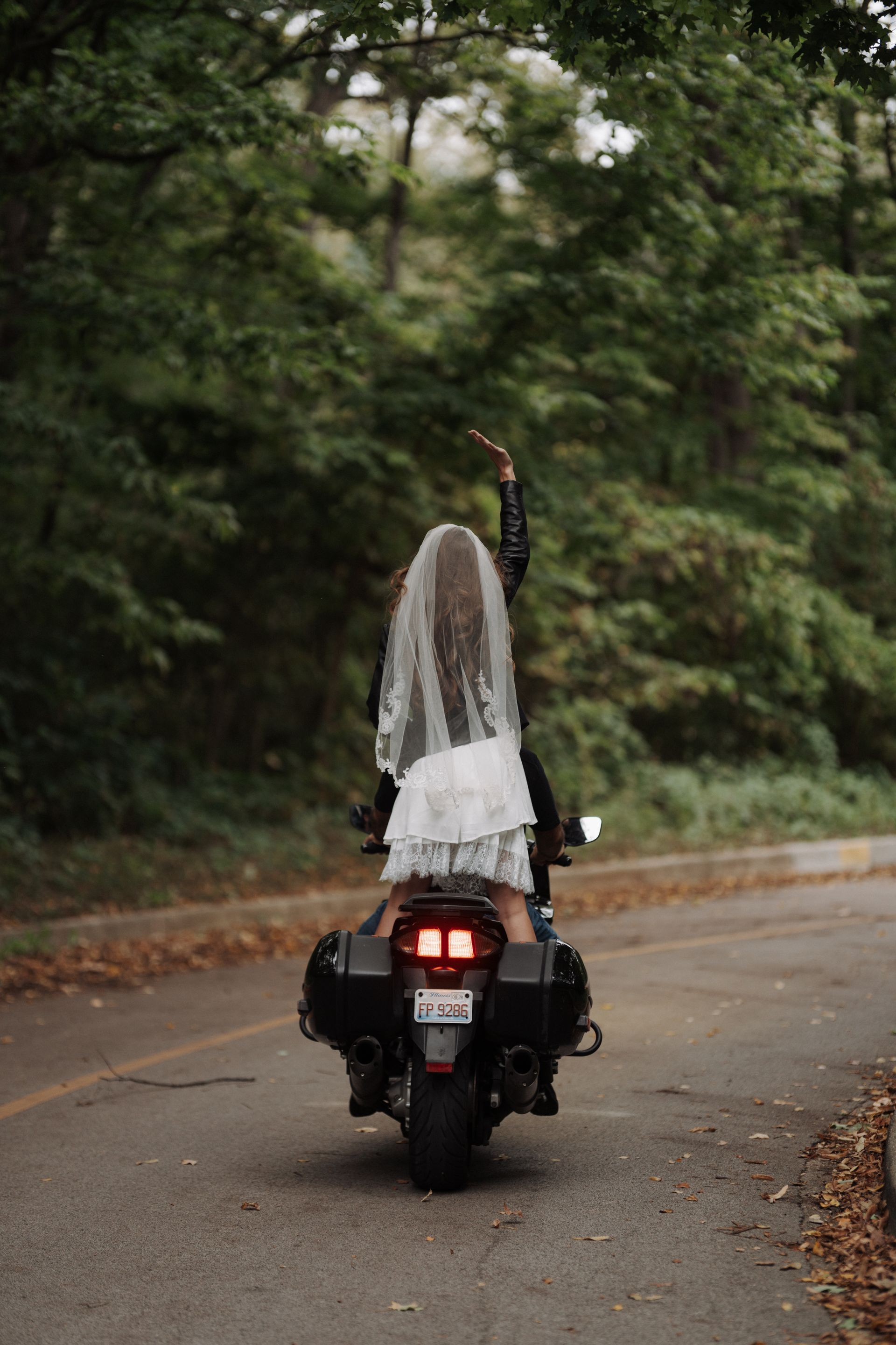 Bride and groom embracing, she smiles at him while he whispers, wearing formal wedding attire; outdoors.