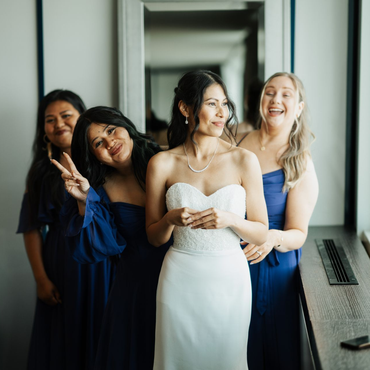 Bride in white dress with three bridesmaids in blue dresses; smiling.
