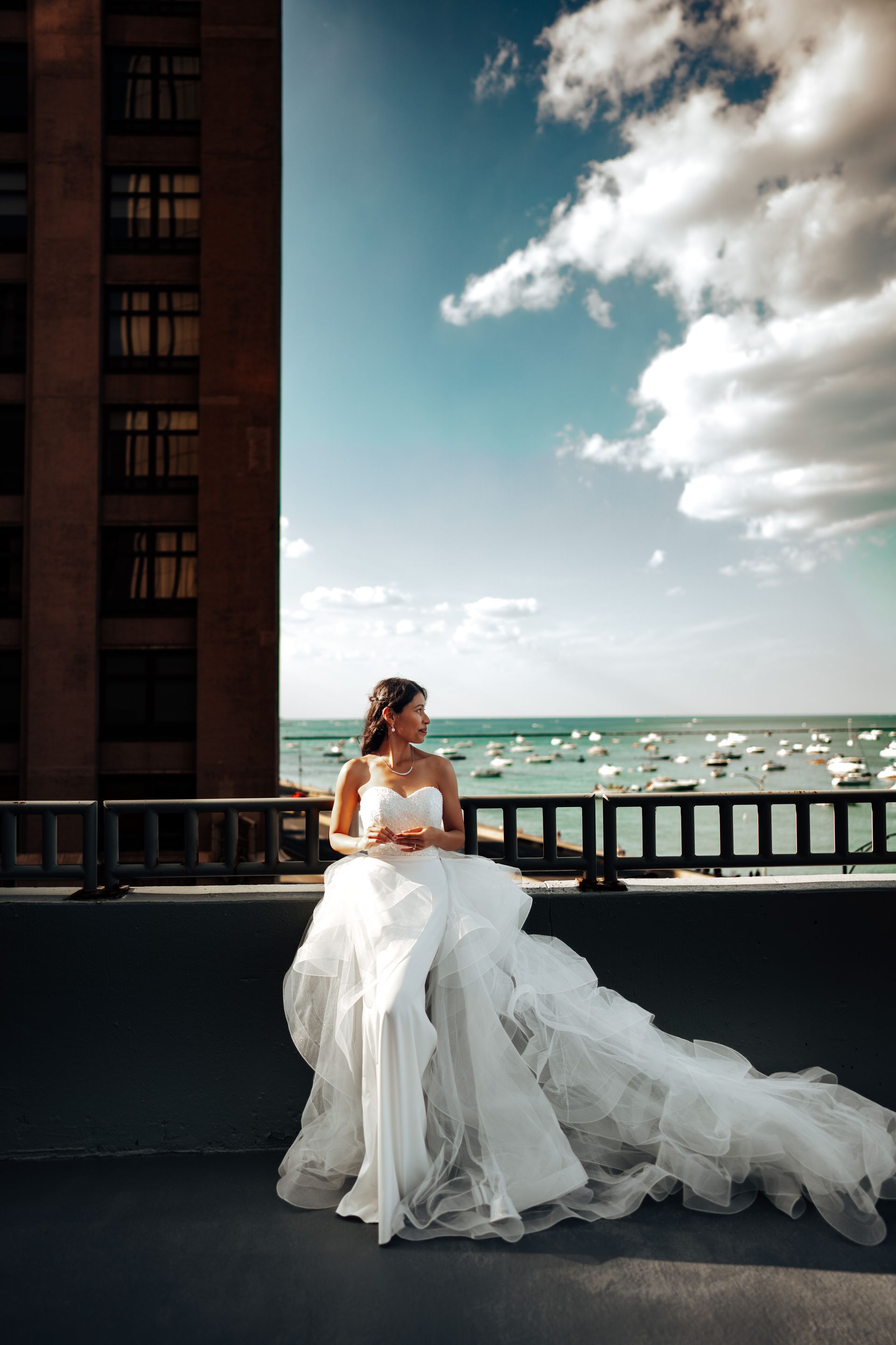 Bride in white wedding dress on rooftop overlooking ocean, blue sky.