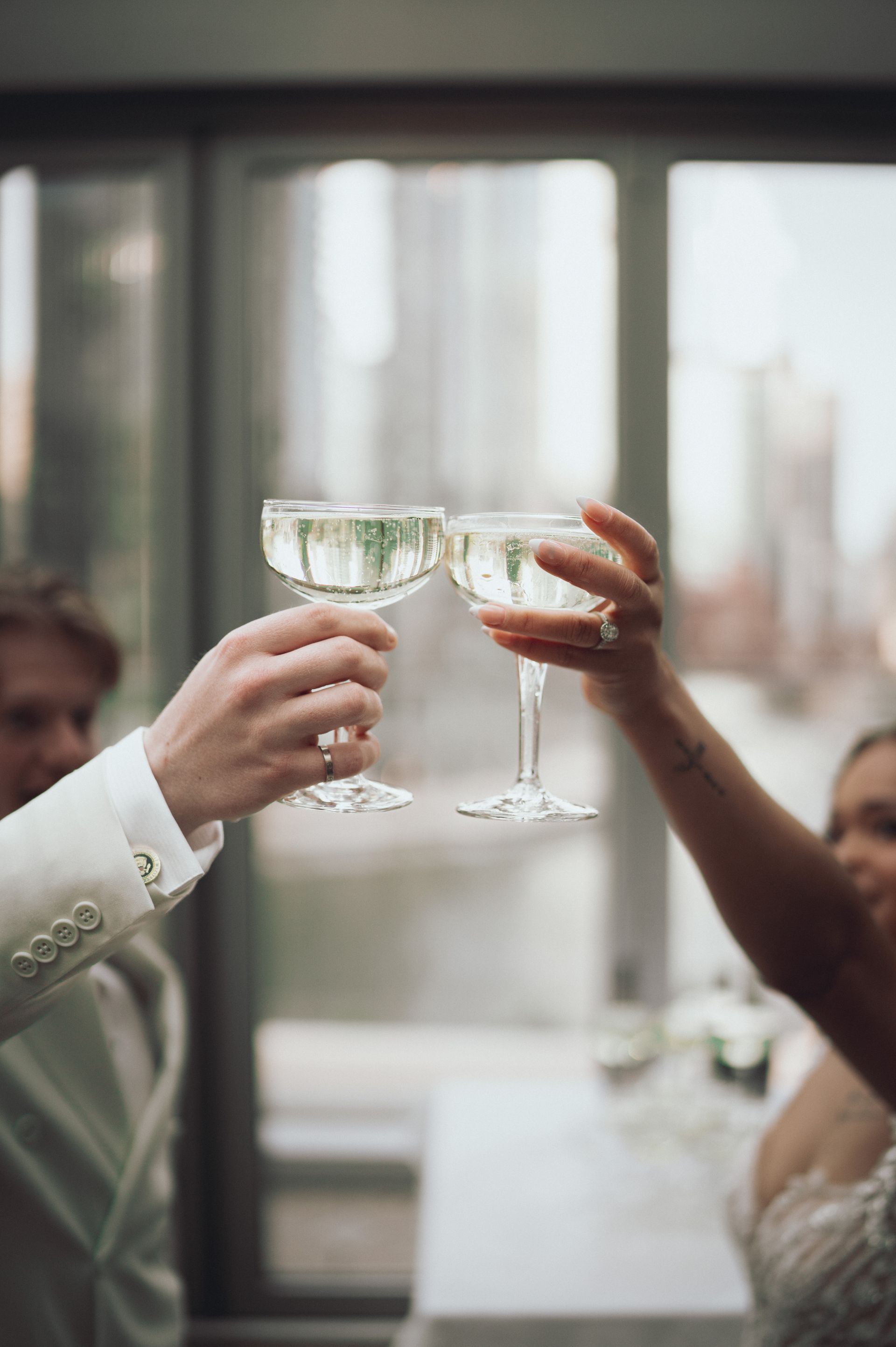 Two people toasting champagne glasses. City background, wearing formal attire.