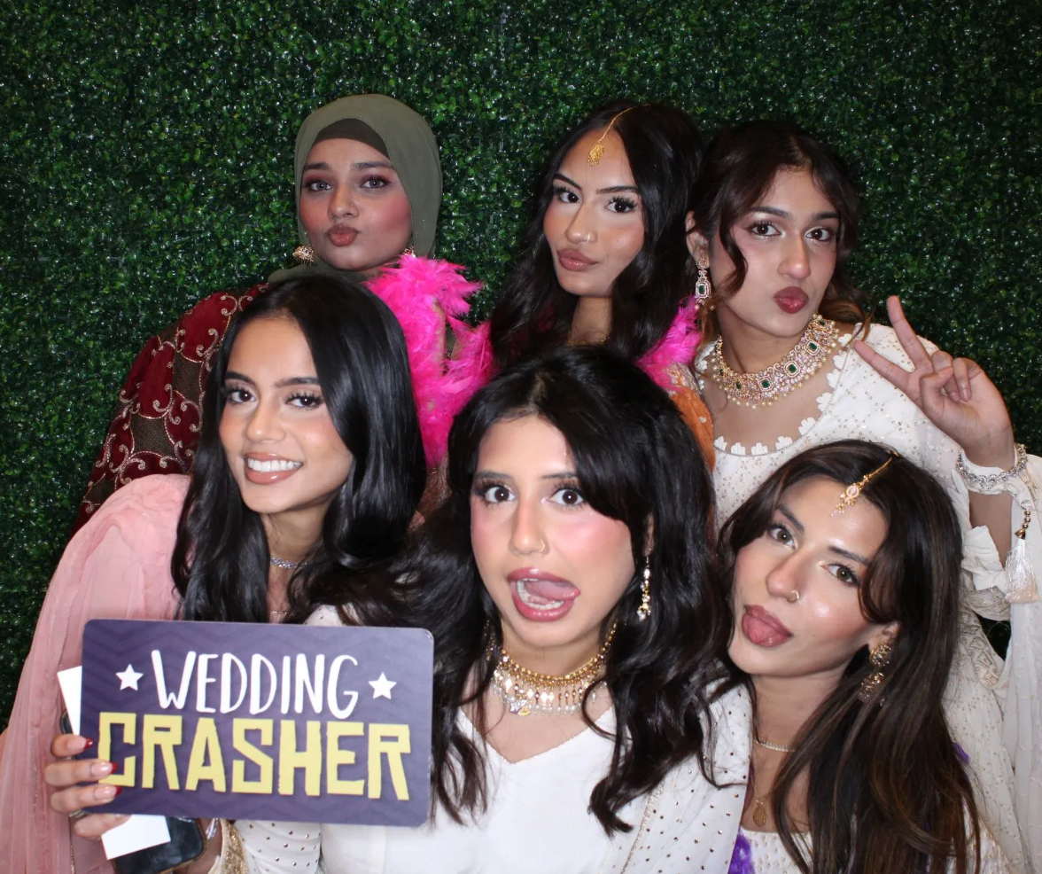 Couple wearing pink heart-shaped glasses at a wedding reception. Woman smiles, touching man's face.